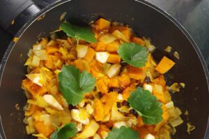 In einer Pfanne ist ein Gericht zu sehen aus Kürbis und Kohl, Darauf sind Gundermannblätter.